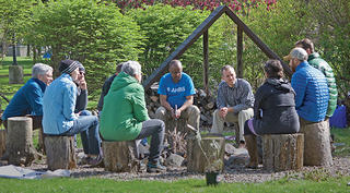 Group of people sit on stumps around a fire circle outside